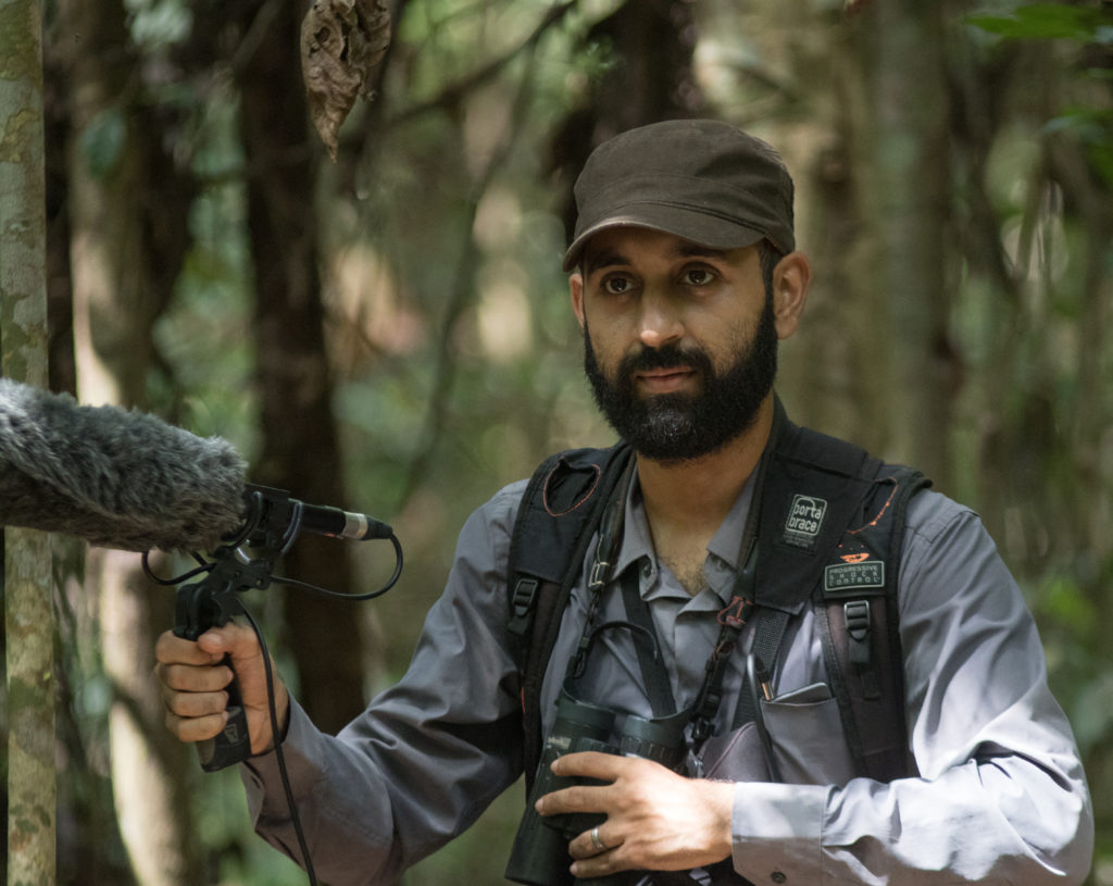 Pablo Cerqueira with his equipments, a shotgun microphone and binoculars inside the forest.